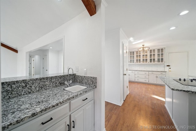 kitchen with backsplash, light stone countertops, white cabinetry, and sink