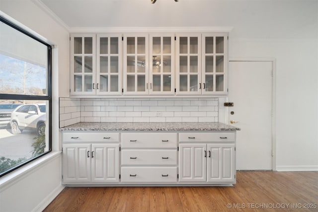 bar with decorative backsplash, light stone counters, crown molding, white cabinets, and light hardwood / wood-style floors