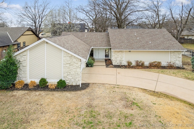 view of front of property featuring stone siding, a shingled roof, and fence