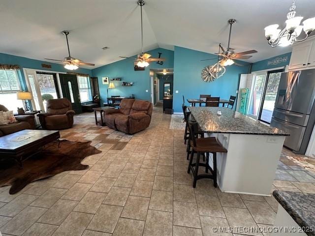 kitchen featuring a kitchen breakfast bar, vaulted ceiling, dark stone countertops, white cabinetry, and stainless steel refrigerator