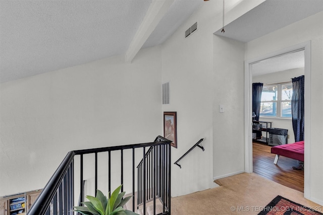 stairway featuring a textured ceiling, carpet floors, and beamed ceiling