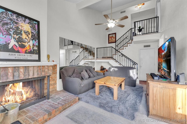 living room with ceiling fan, beamed ceiling, a towering ceiling, and a fireplace