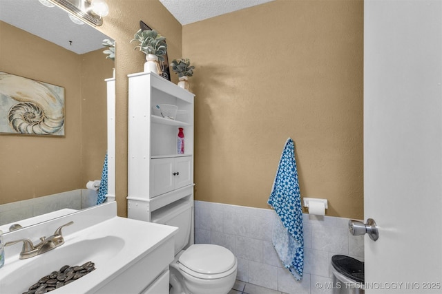 bathroom with a textured ceiling, tile walls, vanity, and toilet