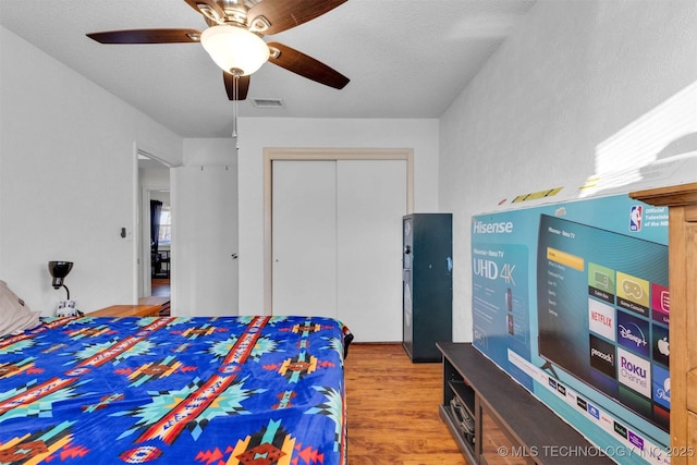 bedroom with a textured ceiling, wood-type flooring, ceiling fan, and a closet