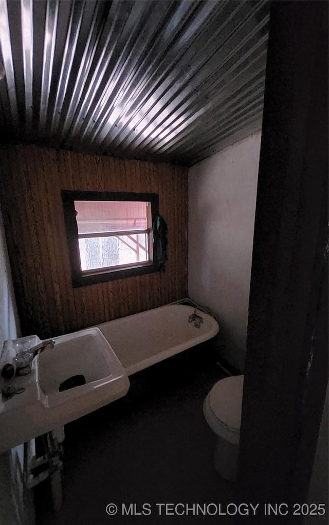 bathroom featuring sink, wood walls, toilet, and a tub to relax in