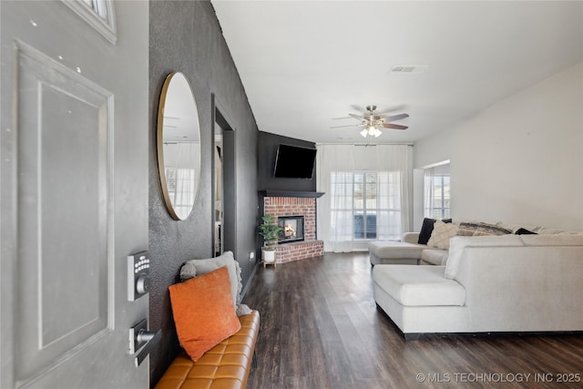 living room featuring ceiling fan, a fireplace, and dark wood-type flooring