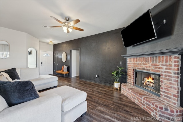 living room featuring ceiling fan, dark hardwood / wood-style flooring, and a brick fireplace