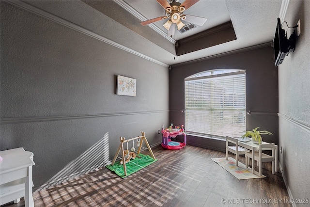 recreation room featuring a tray ceiling, ceiling fan, hardwood / wood-style floors, and ornamental molding