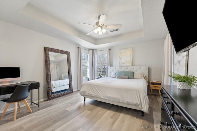 bedroom with ceiling fan, light hardwood / wood-style floors, and a tray ceiling