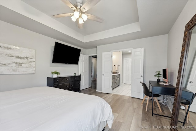 bedroom featuring a tray ceiling, ensuite bath, ceiling fan, and light hardwood / wood-style floors