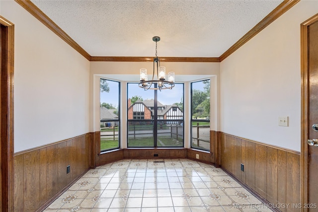 unfurnished dining area with wooden walls, ornamental molding, a textured ceiling, and a notable chandelier