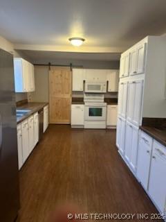 kitchen with white cabinets, white appliances, a barn door, and dark wood-type flooring