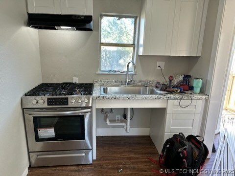 kitchen with stainless steel range with gas stovetop, white cabinets, light stone countertops, dark wood-type flooring, and sink