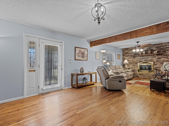 living room featuring a brick fireplace, a textured ceiling, ceiling fan, beamed ceiling, and light hardwood / wood-style floors