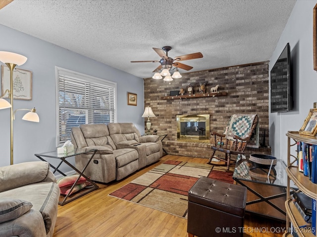 living room with ceiling fan, a fireplace, light wood-type flooring, and a textured ceiling