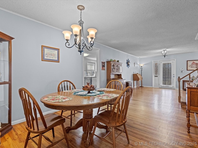 dining space featuring light hardwood / wood-style floors, ornamental molding, a textured ceiling, and a chandelier