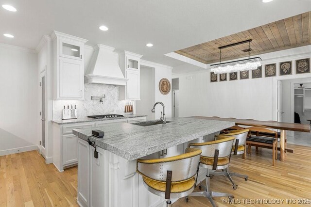 kitchen featuring white cabinetry, sink, hanging light fixtures, premium range hood, and a center island with sink