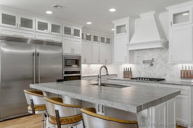 kitchen featuring white cabinets, a kitchen breakfast bar, sink, built in appliances, and custom range hood