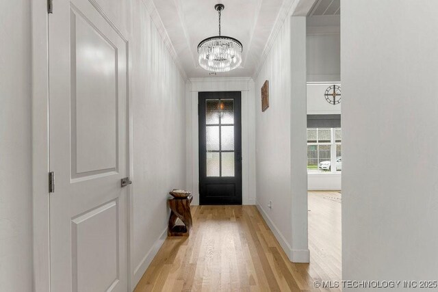 doorway to outside featuring light wood-type flooring, ornamental molding, and a chandelier