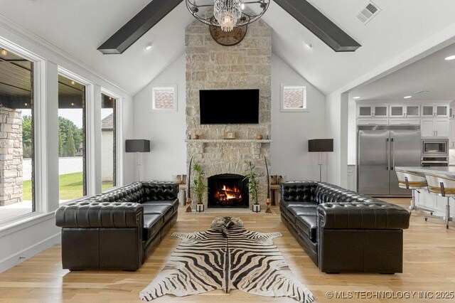 living room featuring lofted ceiling with beams, light hardwood / wood-style floors, and a stone fireplace