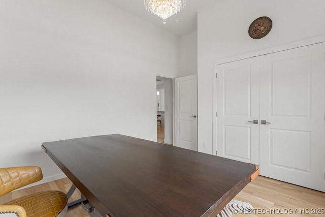 office area with light hardwood / wood-style flooring, a towering ceiling, and a chandelier