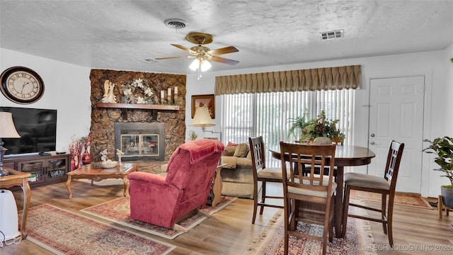 living room with hardwood / wood-style flooring, ceiling fan, a fireplace, and a textured ceiling