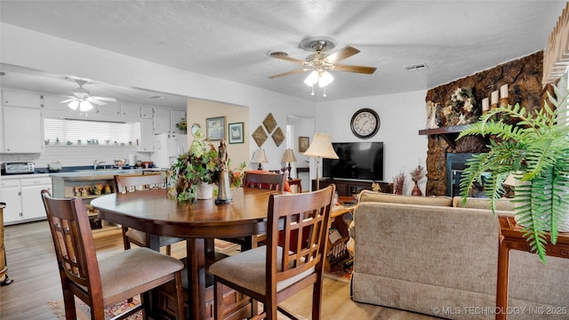 dining area featuring ceiling fan, sink, a fireplace, and light hardwood / wood-style flooring