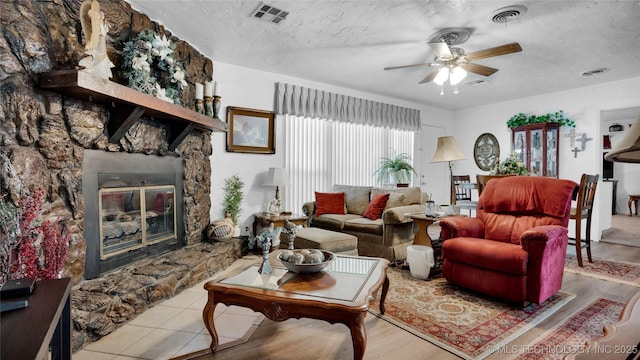 living room with a fireplace, a textured ceiling, light hardwood / wood-style floors, and ceiling fan