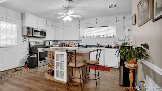 kitchen with ceiling fan, white cabinetry, a kitchen breakfast bar, a kitchen island, and appliances with stainless steel finishes