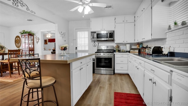 kitchen with white cabinets, light hardwood / wood-style flooring, decorative backsplash, a kitchen island, and stainless steel appliances