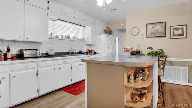 kitchen with a kitchen island, white cabinetry, sink, and white refrigerator with ice dispenser