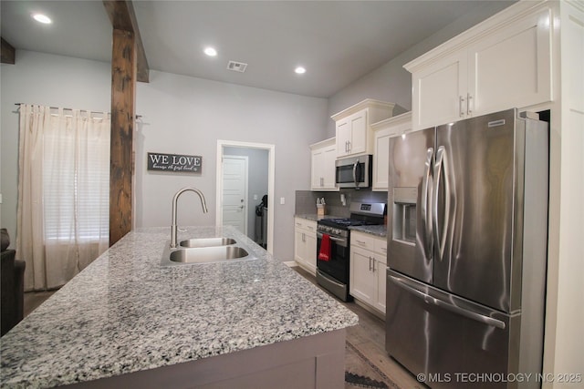 kitchen featuring a center island with sink, light stone counters, sink, and stainless steel appliances