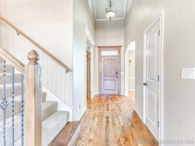 foyer entrance with light wood-type flooring, ornamental molding, and a towering ceiling