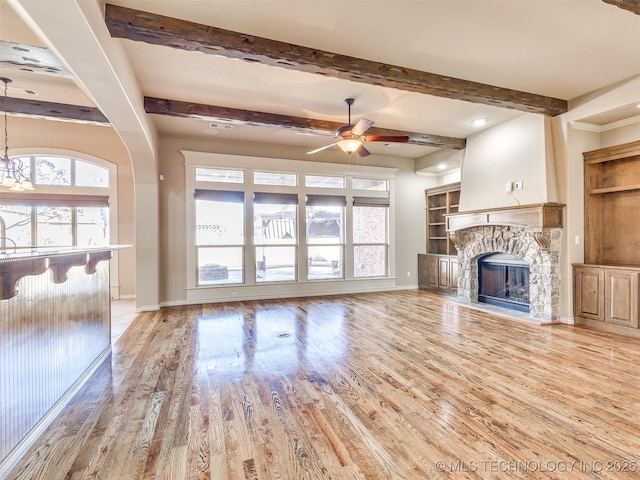 unfurnished living room with a fireplace, light hardwood / wood-style floors, ceiling fan, and beamed ceiling