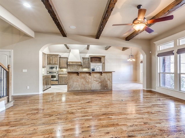 unfurnished living room featuring light wood-type flooring, beam ceiling, and ceiling fan with notable chandelier