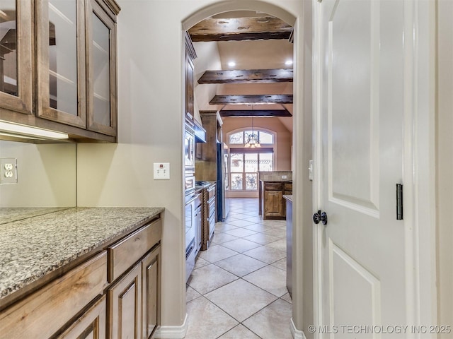 kitchen with stainless steel fridge, light tile patterned floors, beam ceiling, light stone counters, and a chandelier