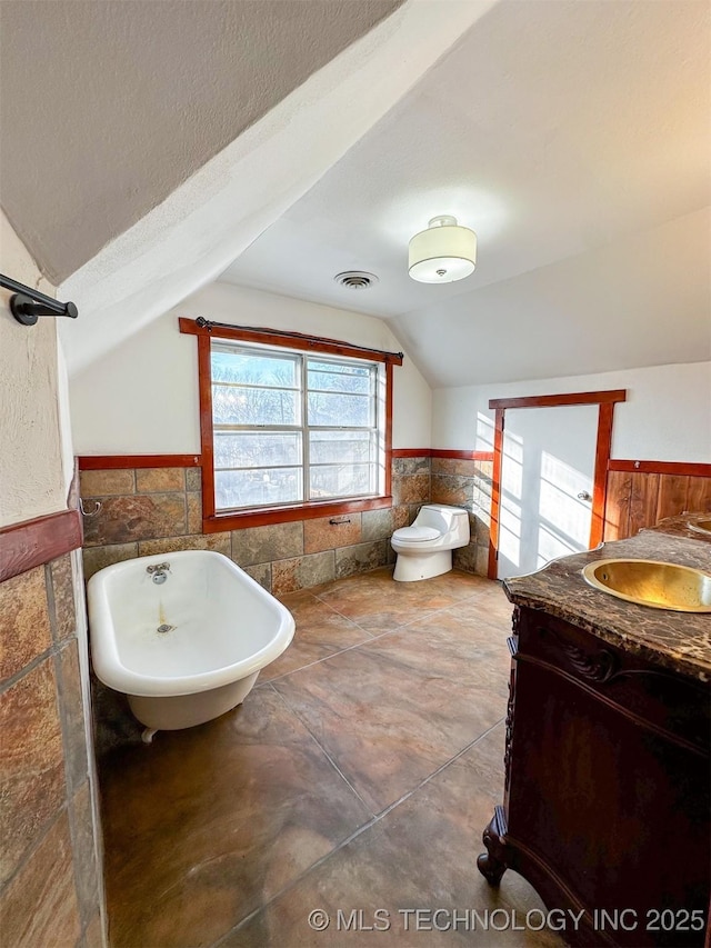 bathroom with vanity, a bathing tub, vaulted ceiling, toilet, and tile walls