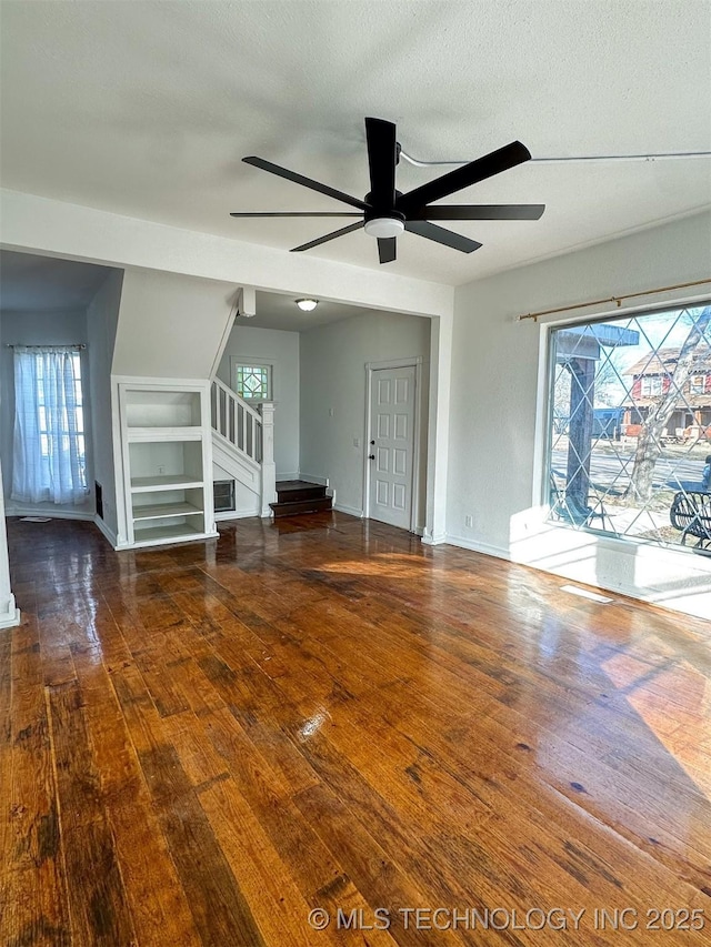 unfurnished living room featuring built in shelves, a textured ceiling, dark hardwood / wood-style floors, and ceiling fan