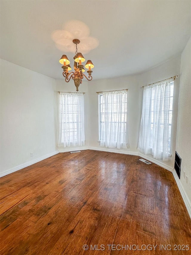 spare room featuring wood-type flooring and an inviting chandelier