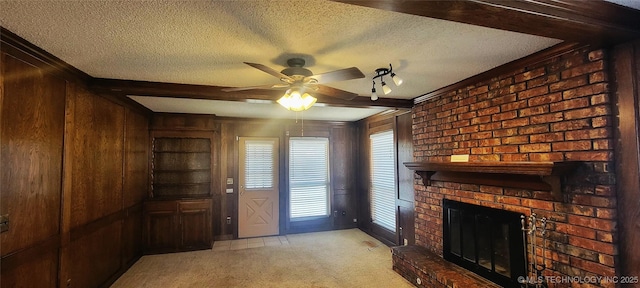 unfurnished living room featuring ceiling fan, light carpet, a textured ceiling, wooden walls, and a fireplace