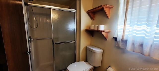 bathroom featuring a shower with door and toilet