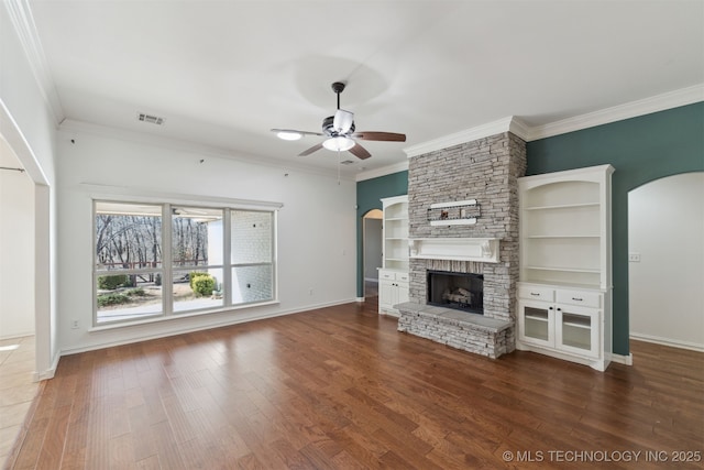 unfurnished living room with built in shelves, ceiling fan, a stone fireplace, hardwood / wood-style flooring, and ornamental molding