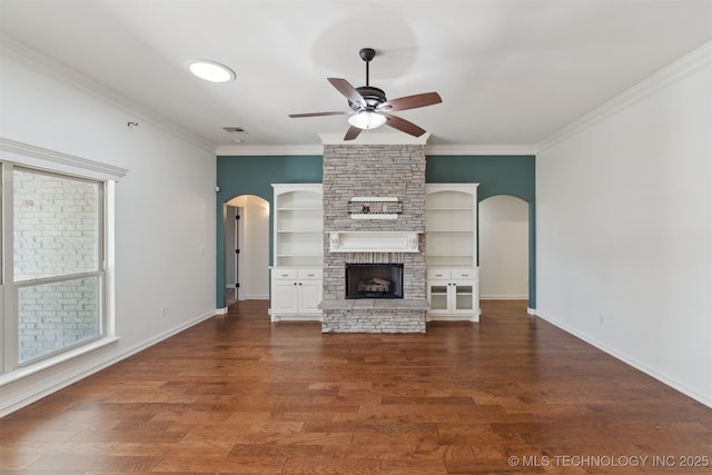 unfurnished living room featuring ceiling fan, dark wood-type flooring, a stone fireplace, plenty of natural light, and ornamental molding