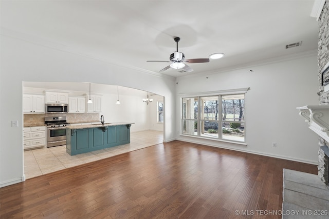 unfurnished living room featuring sink, light wood-type flooring, a fireplace, ceiling fan with notable chandelier, and ornamental molding