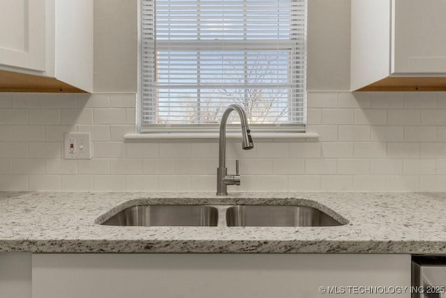 kitchen with decorative backsplash, white cabinetry, sink, and light stone counters