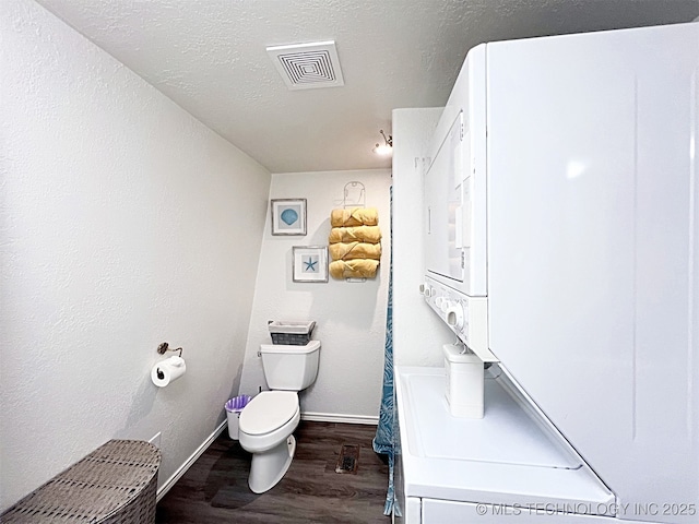 bathroom featuring hardwood / wood-style flooring, stacked washer / drying machine, toilet, and a textured ceiling