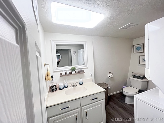 bathroom featuring vanity, hardwood / wood-style flooring, toilet, a textured ceiling, and washer / dryer