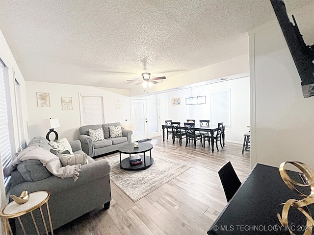 living room with ceiling fan, a textured ceiling, and light wood-type flooring