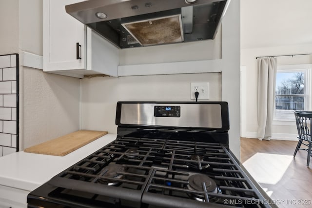 interior space with white cabinetry, exhaust hood, and gas range