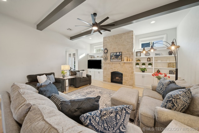 living room with light wood-type flooring, built in shelves, ceiling fan, beam ceiling, and a fireplace